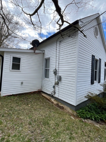 technician soft washing vinyl siding on a shaded West Asheville home